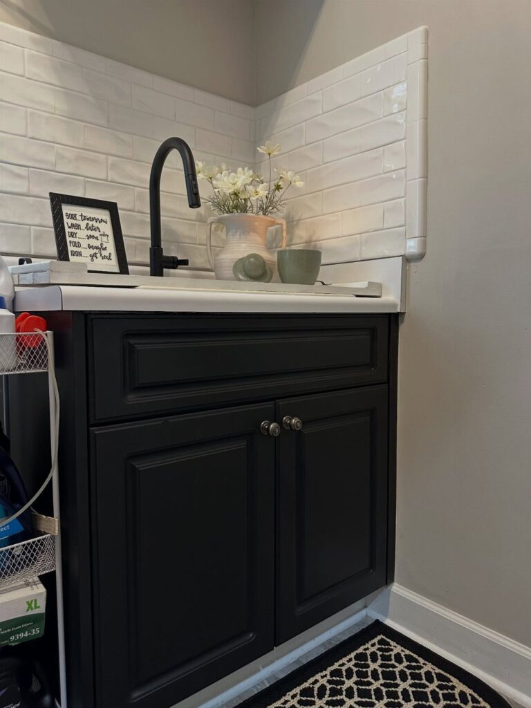 White subway tile backsplash behind a black faucet and navy blue laundry cabinets.