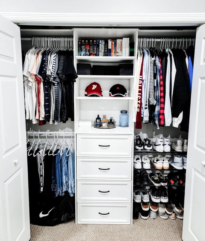 Organized white closet with hanging clothes, central drawers, shelving, and a shoe rack.