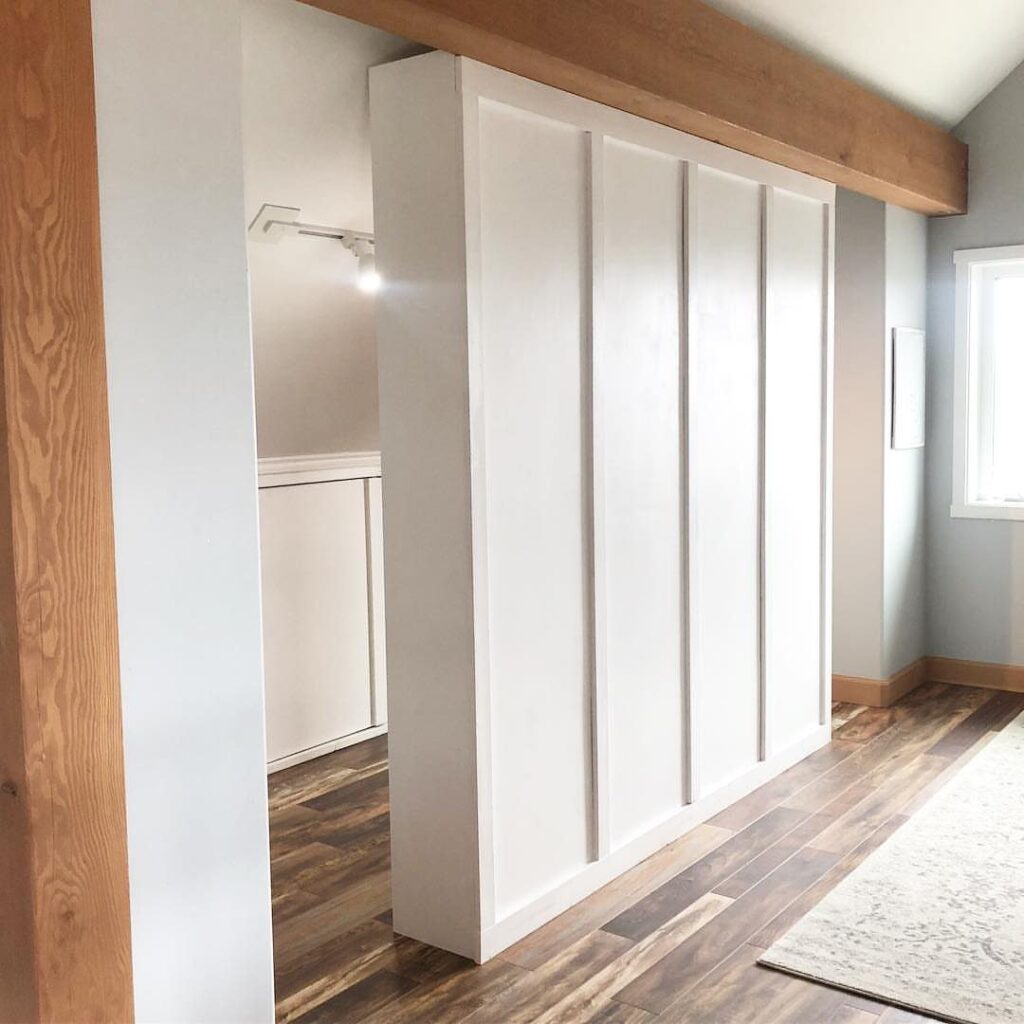 White built-in closet system serving as a room divider with wooden ceiling beams.