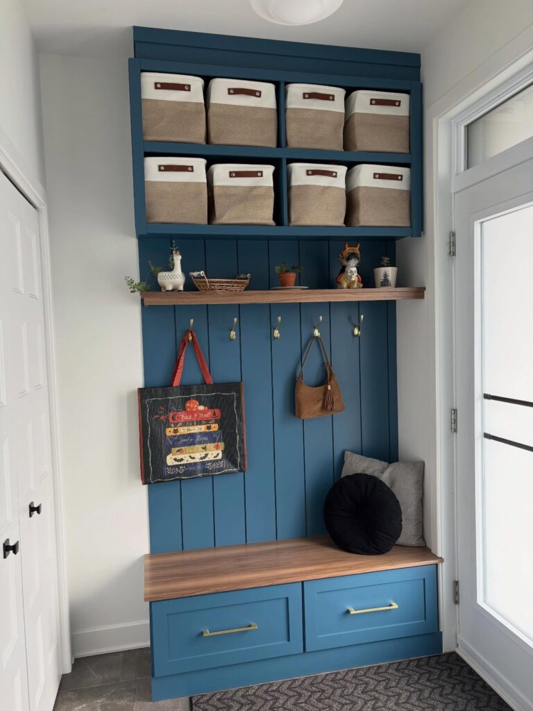 Blue built-in mudroom bench with wooden seat, storage drawers, and upper cubby bins.