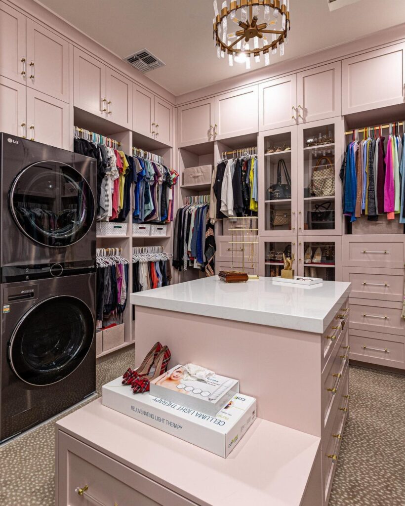 Stacked black washer and dryer integrated into a pale pink luxury walk-in closet
