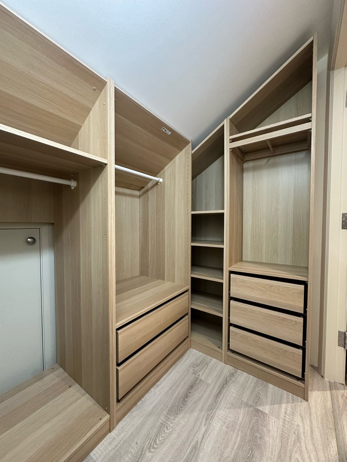 Light wood built-in closet with shelves and drawers under a slanted white ceiling.