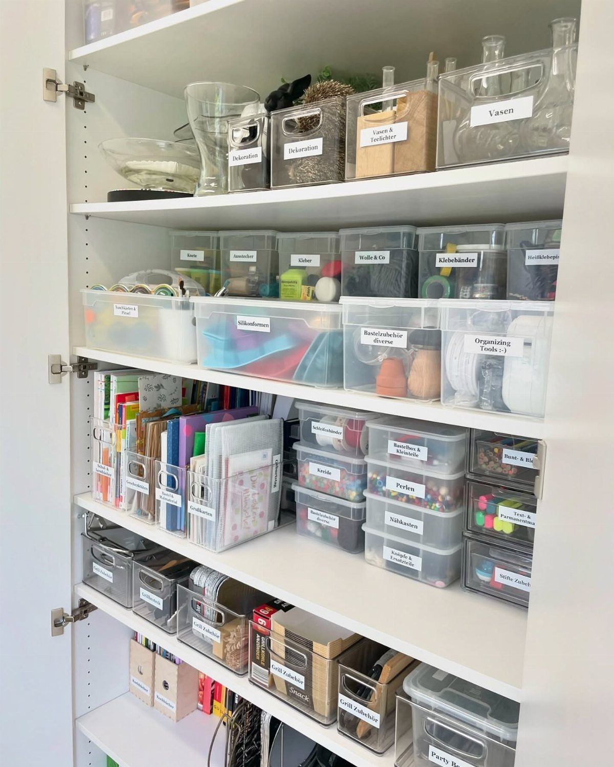 Clear plastic storage bins organized on white shelves containing various craft supplies.