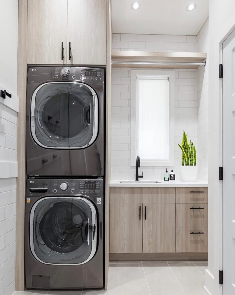 Stacked dark grey washer and dryer in a small laundry room with wood cabinets.