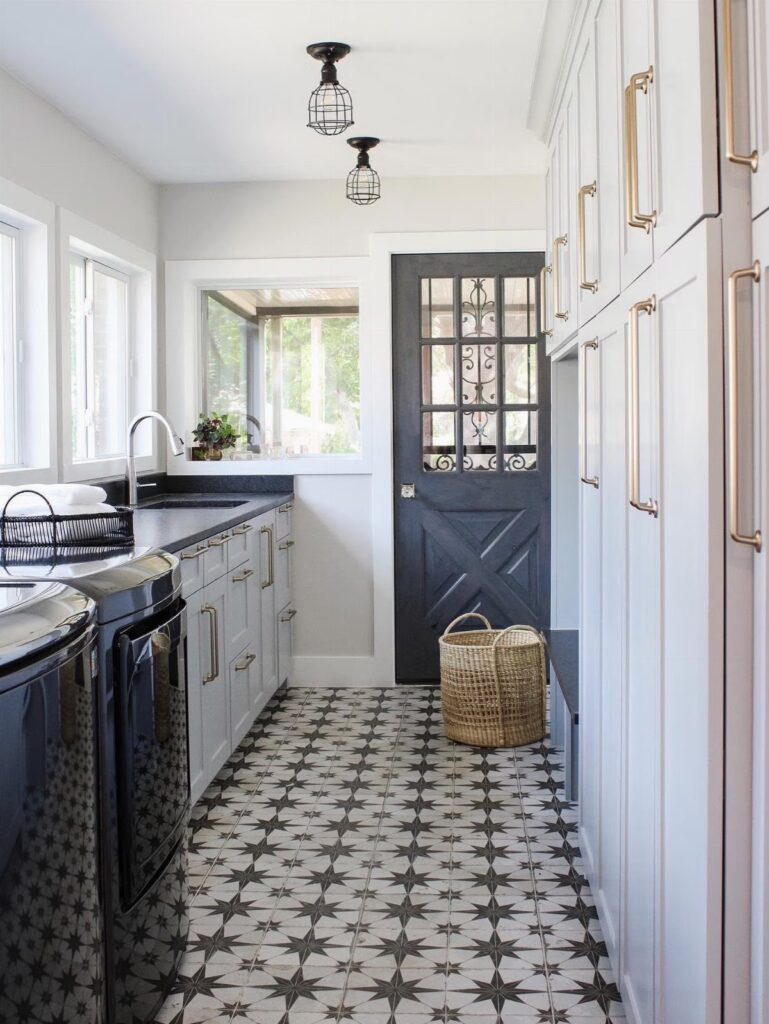 Laundry room with black machines, grey cabinets, and patterned black and white tiles.