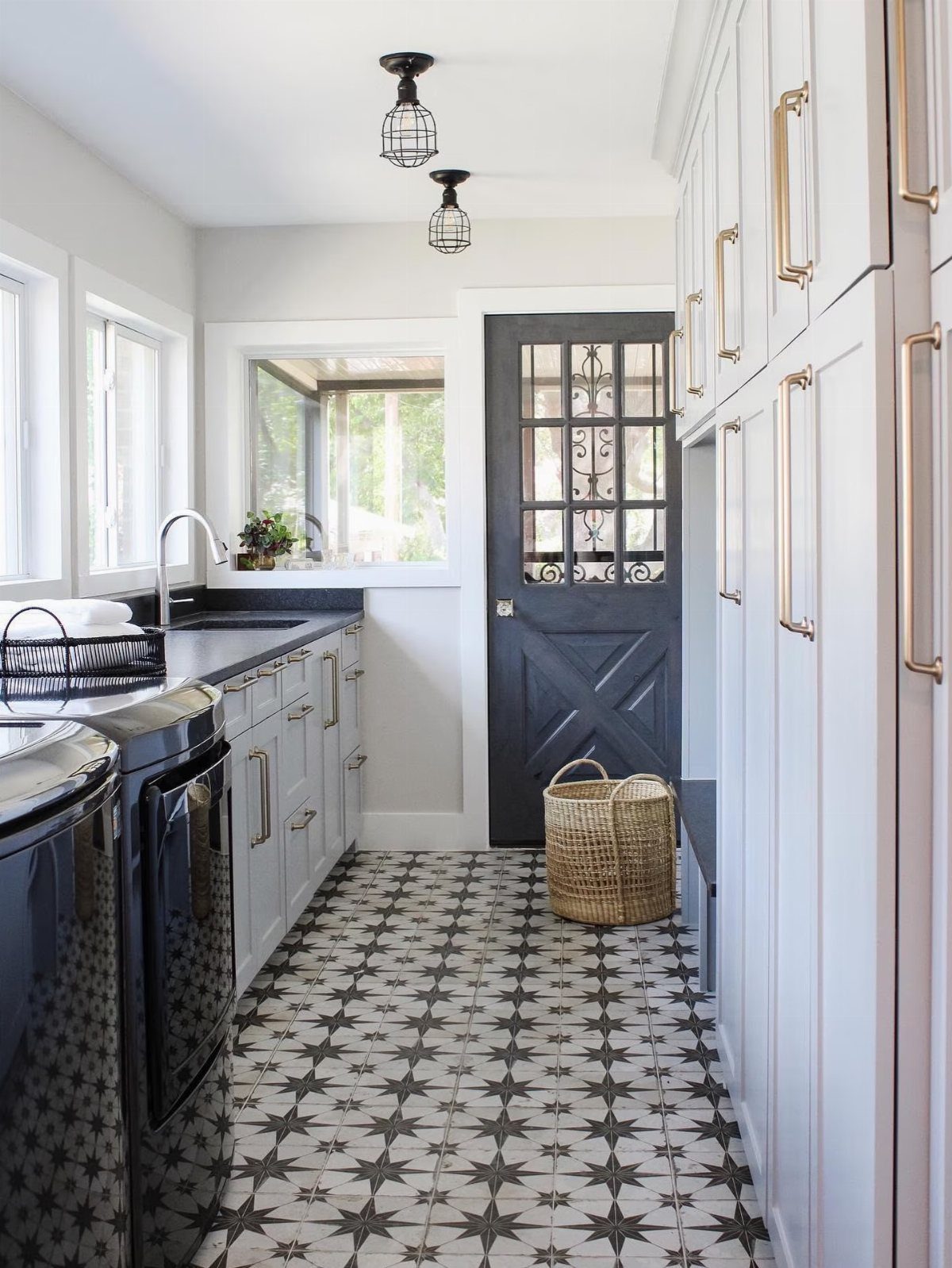 Laundry room with black machines, grey cabinets, and patterned black and white tiles.