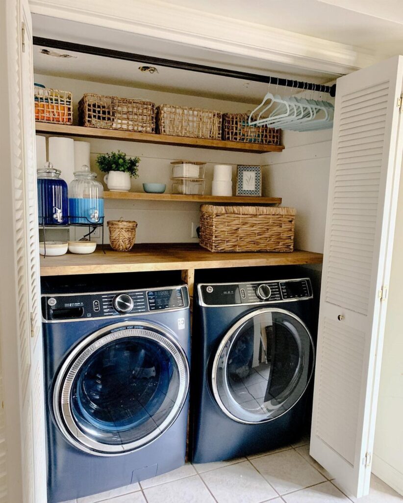 Blue washer and dryer with wooden shelves holding organized baskets and detergent jars.