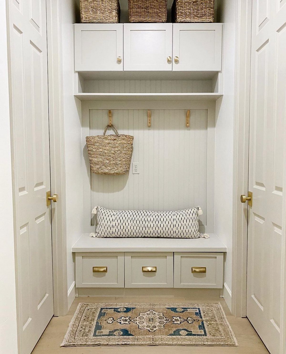 White built-in mudroom nook with bench, storage drawers, and upper cabinets in small space.