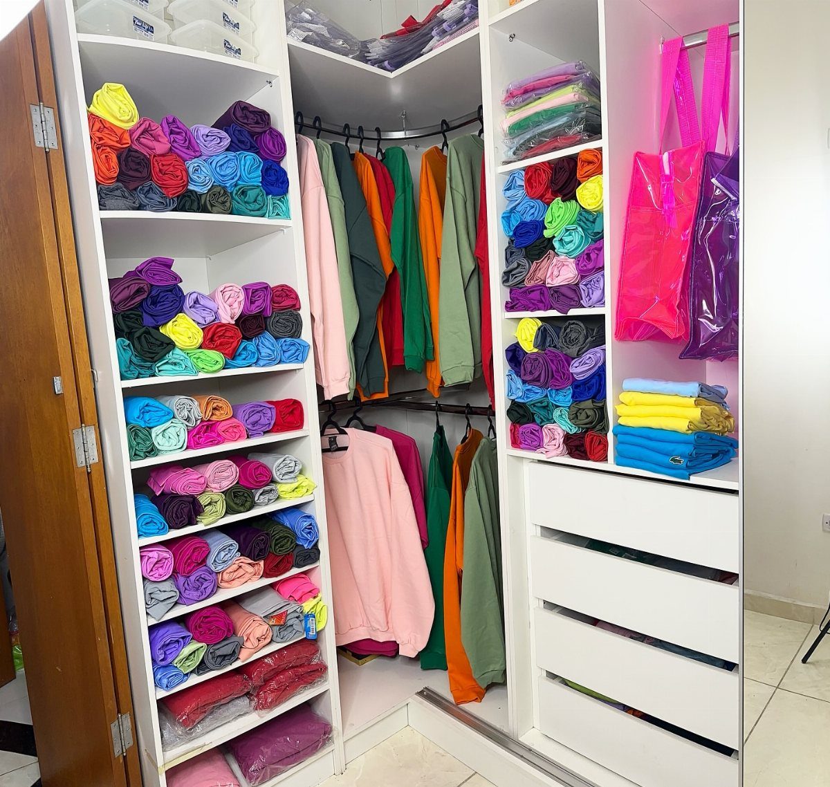 Colorful clothes organized by color on shelves and hanging rods in a white closet.