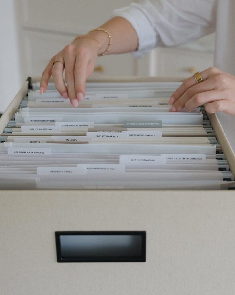 Hands organizing labeled translucent hanging folders inside a light-colored filing cabinet drawer.