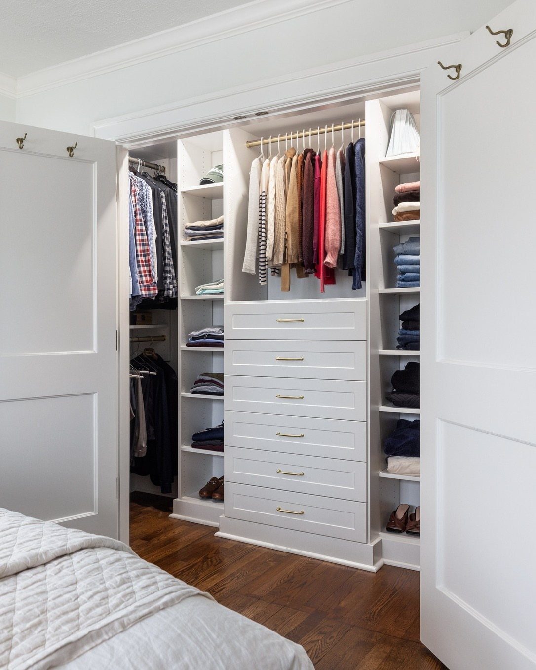 White reach-in closet with built-in drawers, shelves, and hanging clothes on wood floors.