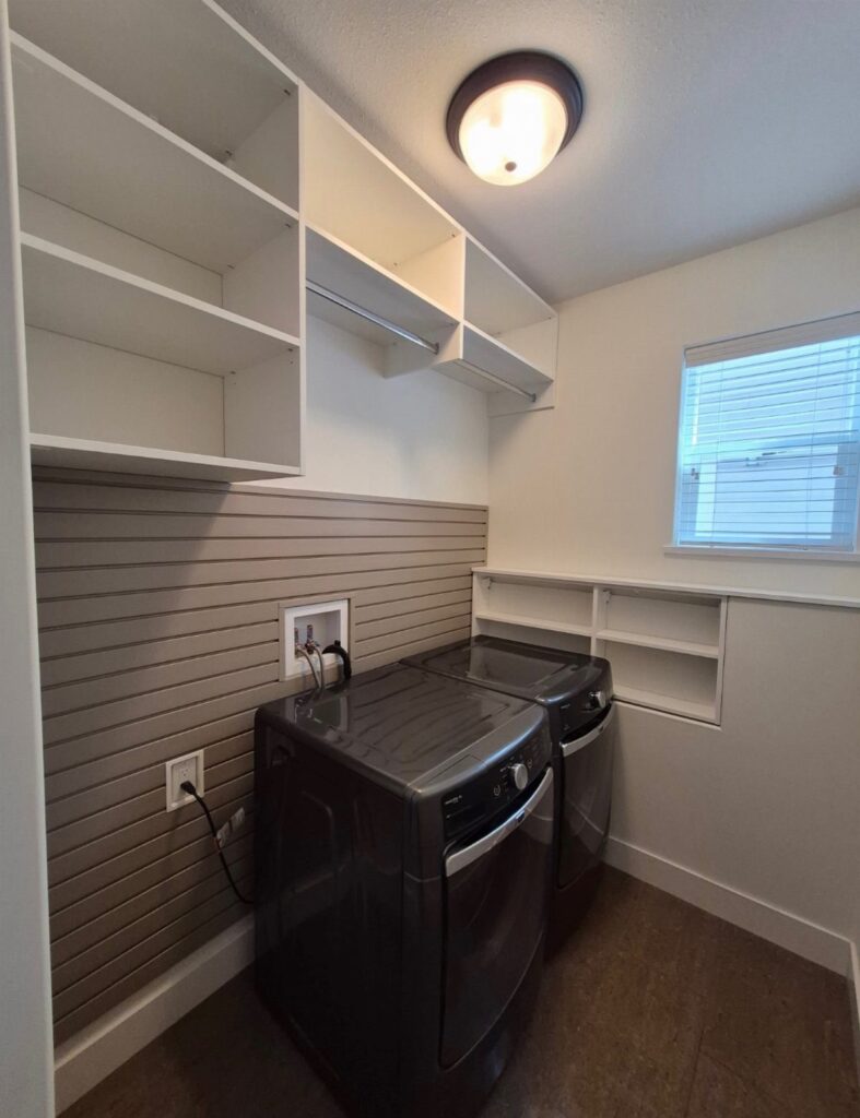 White open shelving installed on the wall above a grey washer and dryer.