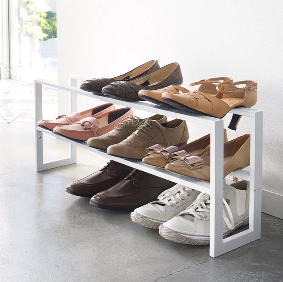 White metal three-tier shoe rack holding various styles of women's shoes against white wall.