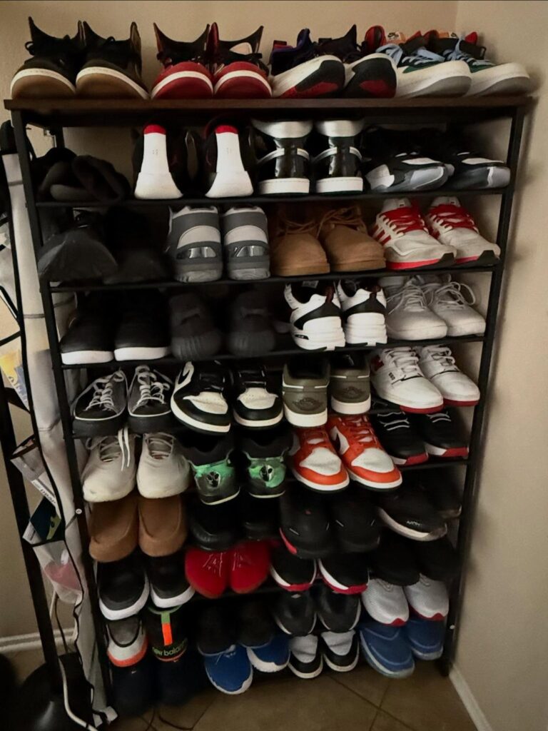Black metal multi-tier shoe rack filled with various sneakers and boots against a wall.