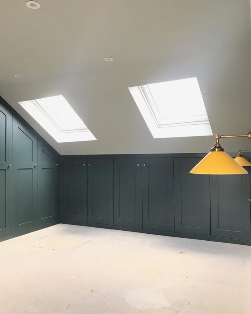 Dark teal knee-wall cabinets built into a slanted attic ceiling with skylights.