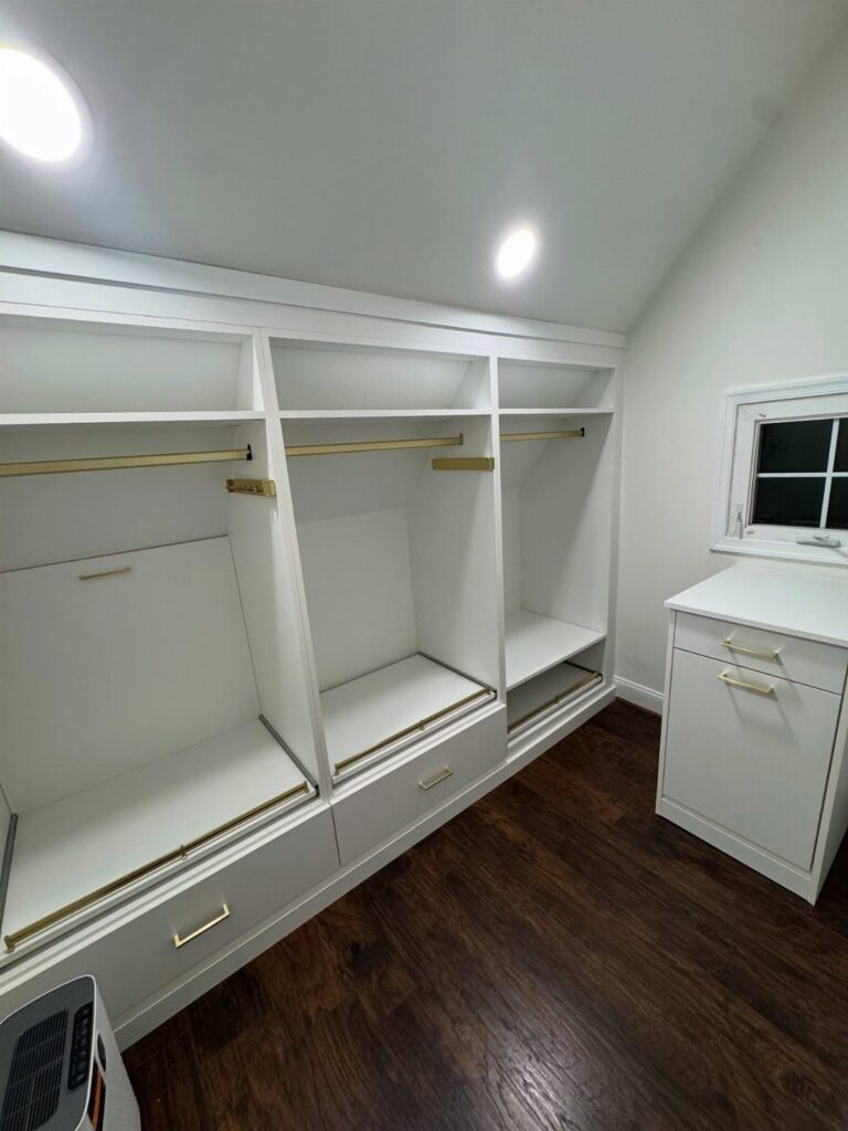 White built-in closet system with drawers and rods under a sloped ceiling