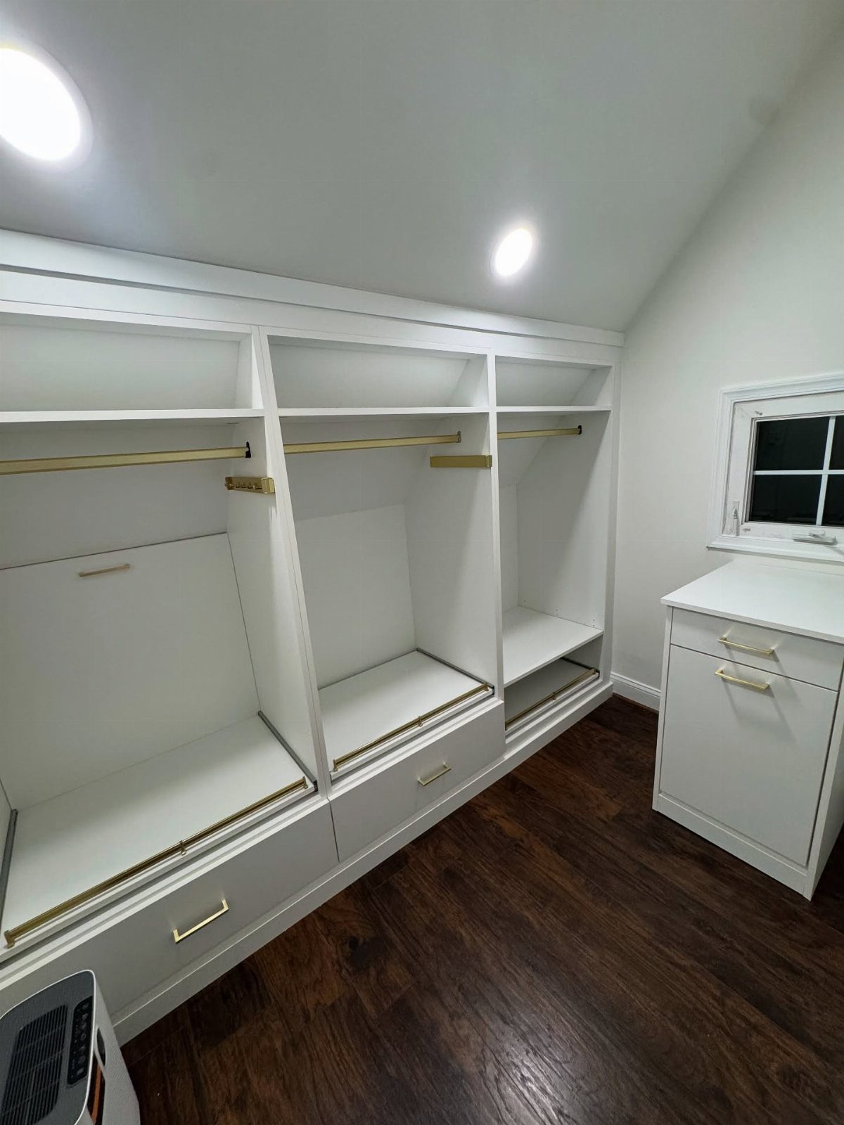 White built-in closet system with drawers and rods under a sloped ceiling