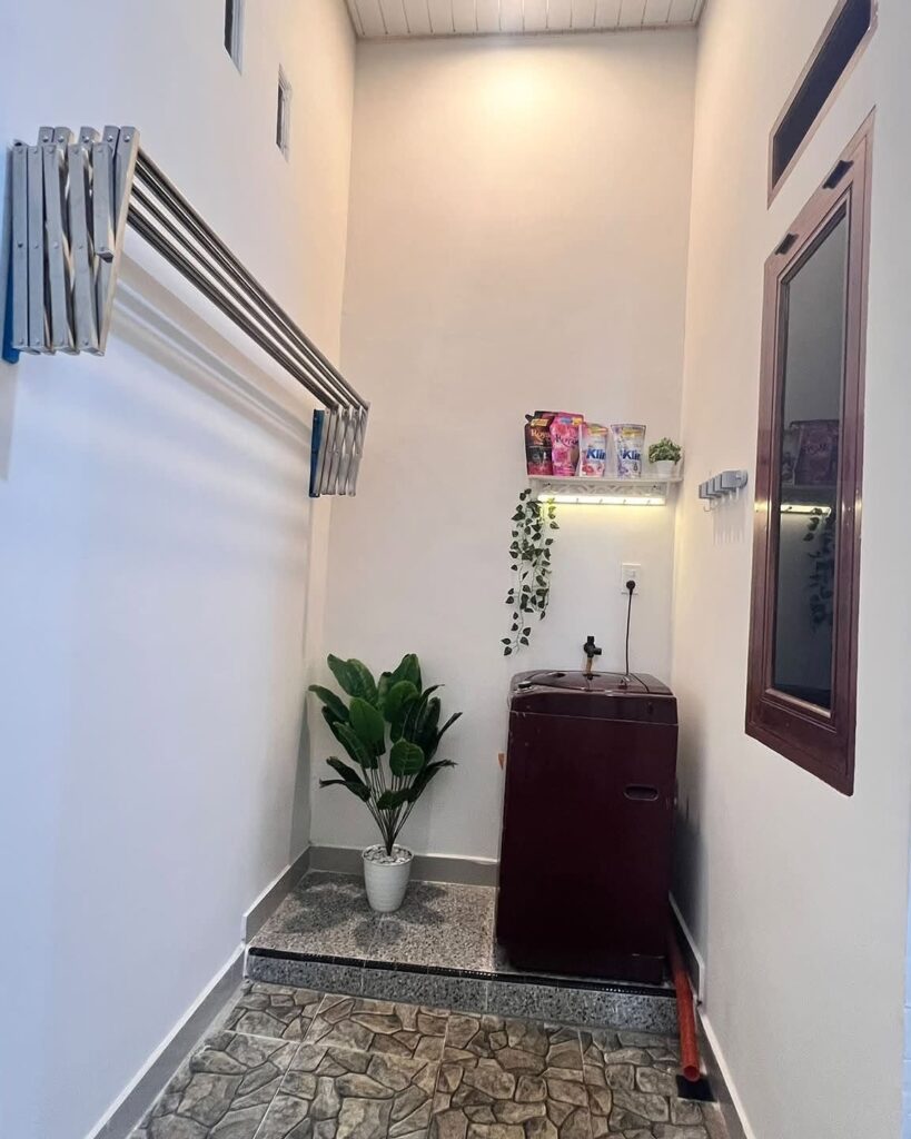 Small laundry area with a brown tub, wall-mounted drying rack, and potted plant.