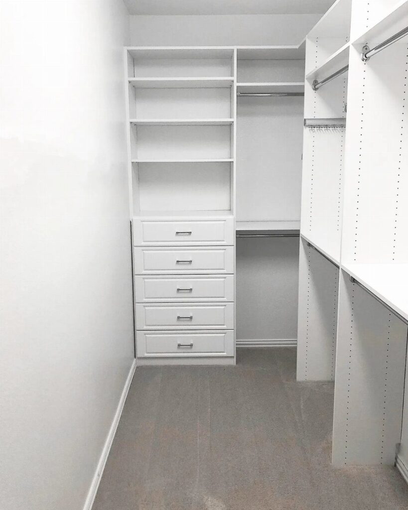 White built-in closet organizer with shelves, drawers, and hanging rods in a small room.