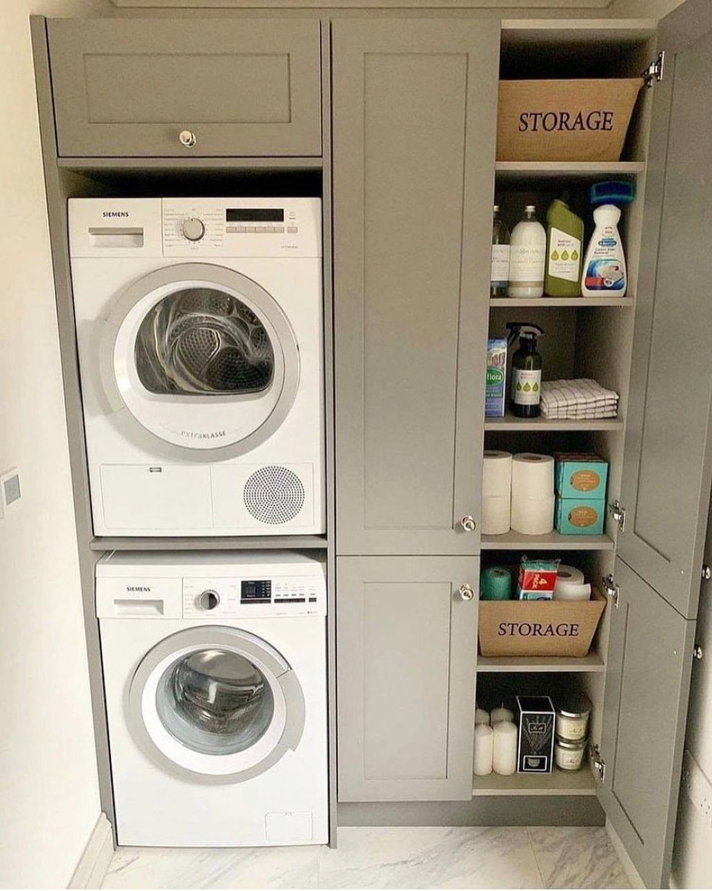 Stackable washer and dryer enclosed in a grey cabinet with side storage shelving.