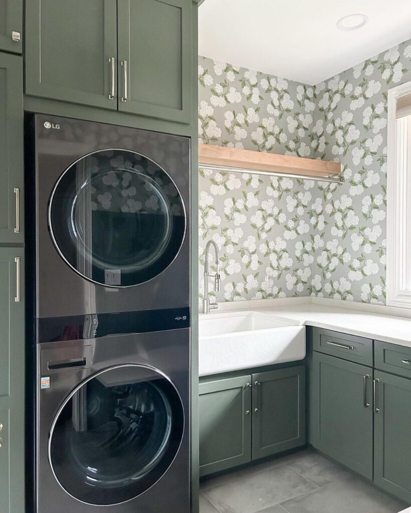 Stacked black washer and dryer next to a sink with floral wallpaper walls.
