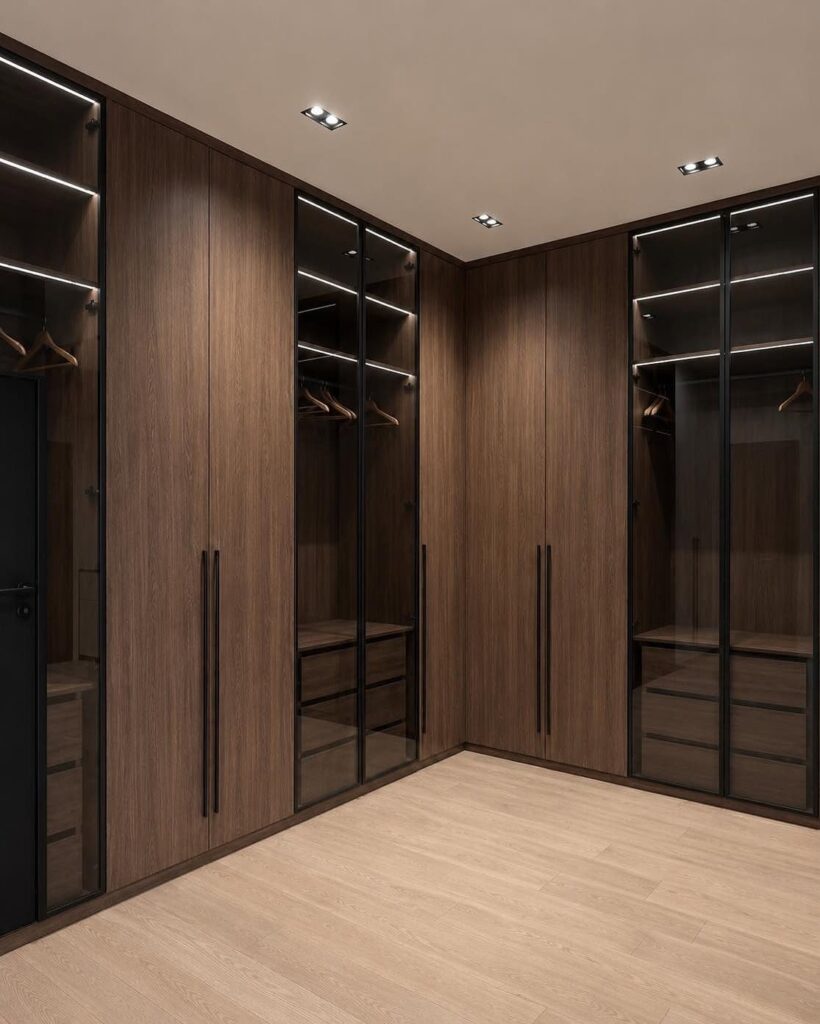 Modern walk-in closet with brown wood cabinets and black glass doors.