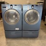 Blue Samsung washer and dryer set elevated on pedestals with pull-out drawers.